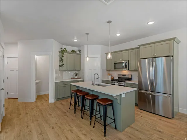 Kitchen featuring wood-finish flooring, recessed lighting, pendant lighting, stainless steel appliances, and an island with an integrated sink
