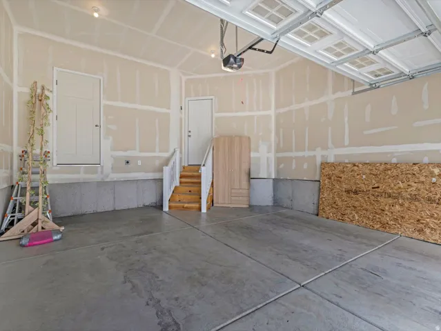 Concrete flooring with expansion joints, unfinished walls, overhead garage door with paneling, built-in staircase with handrail, and recessed lighting