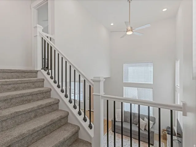 Staircase with carpeted treads and black iron balusters, featuring a high ceiling and recessed lighting