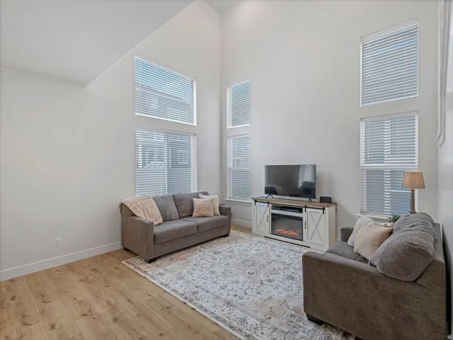 Vaulted ceilings, wood-finish flooring, multiple tall windows with blinds, and a built-in media console with an electric fireplace