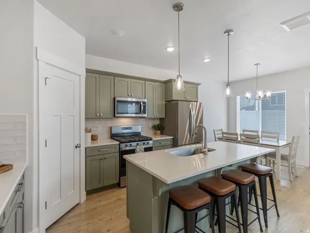 Kitchen featuring sage green cabinetry, stainless steel appliances, light countertops, a kitchen island with sink, and pendant lighting