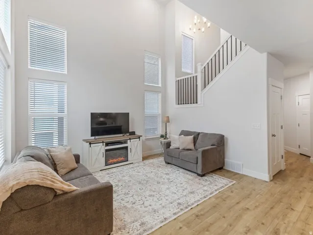 Two-story ceiling height with multiple windows, wood-finish flooring, and an open staircase with metal balusters