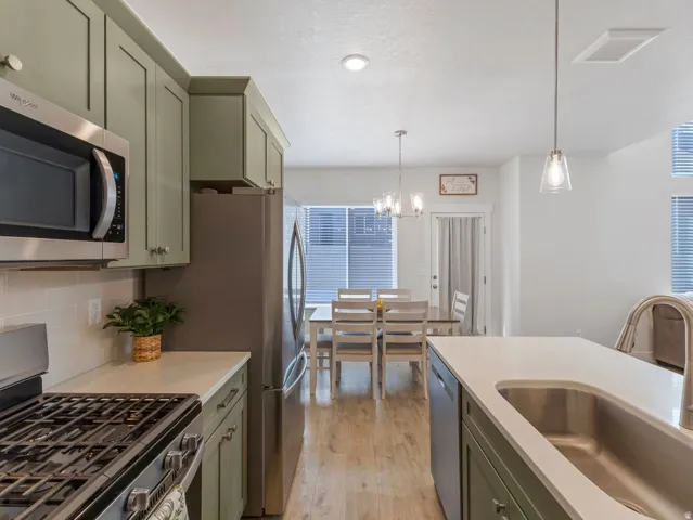 Kitchen featuring sage cabinetry, stainless steel appliances, a tile backsplash, and light countertops