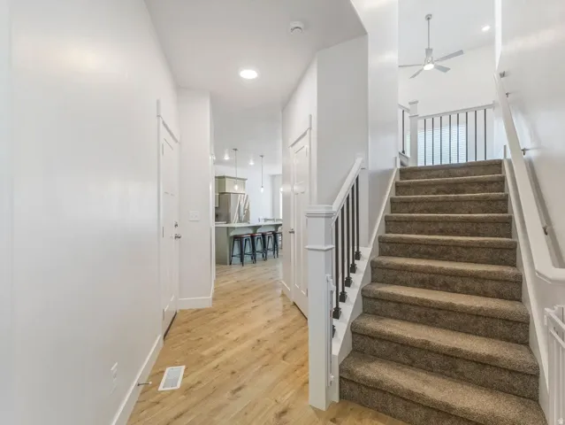 Carpeted staircase with black metal balusters, wood-finish flooring, recessed lighting, and a ceiling fan on the upper level