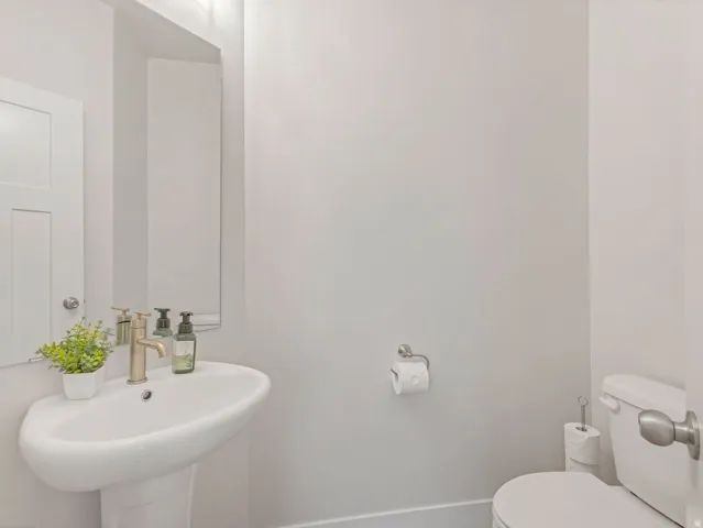 Pedestal sink with a gold-tone faucet, rectangular mirror, and white toilet