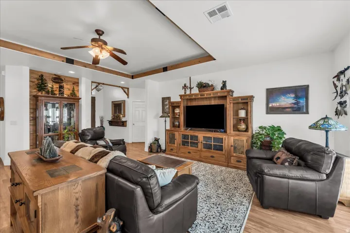 Wood-finish flooring throughout, tray ceiling with wood beam accents, recessed lighting, and a ceiling fan with light fixture