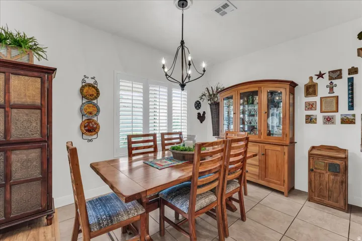 Dining area featuring a chandelier, tile flooring, and windows with plantation shutters
