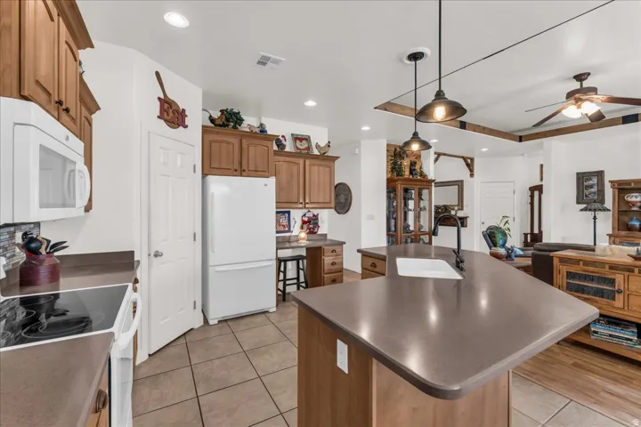 Kitchen featuring wood cabinetry, an island with an undermount sink and dark countertop, recessed lighting, and tile flooring