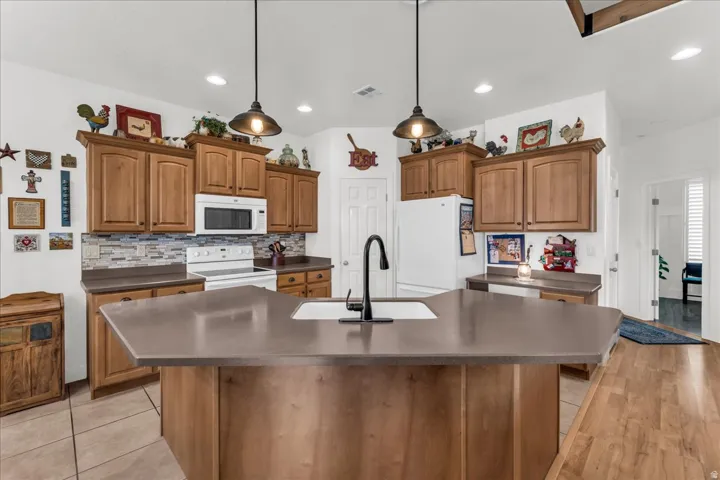 Kitchen featuring wood cabinetry, stone-look countertops, a tile backsplash, and a central island with an undermount sink and matte black faucet