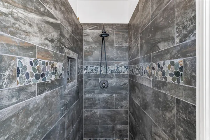 Shower with stone-finish tile surround, decorative pebble tile inlay, built-in shower niche, and matte black shower fixtures