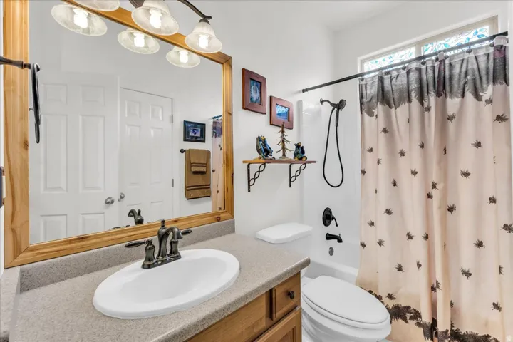 Bathroom featuring a wood-framed mirror, dual-light vanity fixture, an integrated sink with oil-rubbed bronze faucet, a shower/tub combination with dark fixtures, and an upper window with opaque glass
