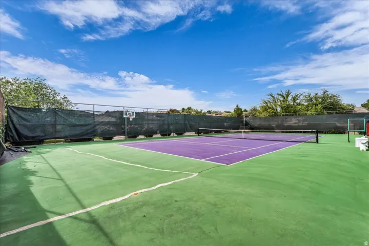 Multi-sport court featuring a tennis net, basketball hoop, and perimeter fencing