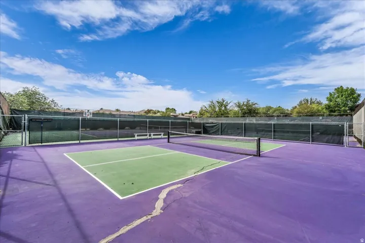 Outdoor court featuring a net, purple and green surface, and perimeter fencing