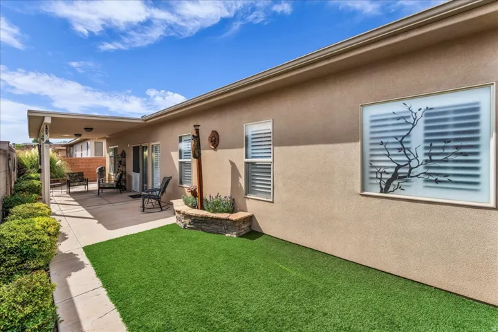 Covered patio with concrete flooring, artificial turf area, stucco exterior, decorative window treatment, and built-in stone planter
