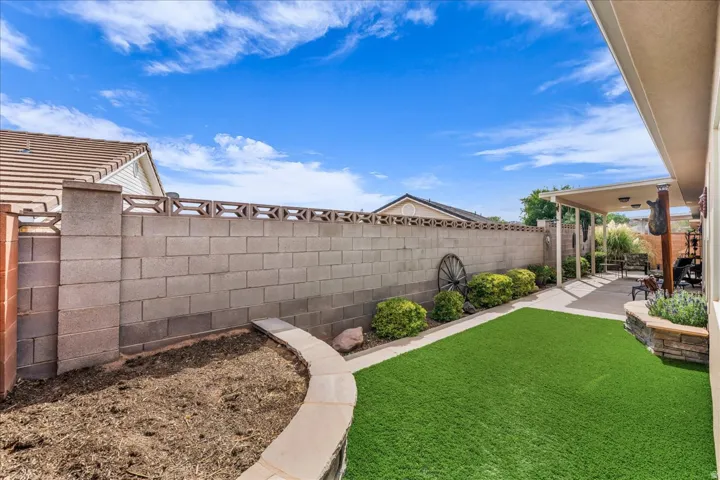Expansive backyard featuring artificial turf, a concrete block privacy wall with decorative elements, a covered patio area, and a stone-clad planter box