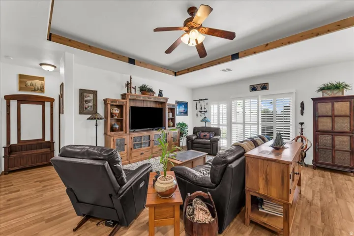 Living area featuring wood-finish flooring, exposed ceiling beams, a ceiling fan, and sliding glass doors with plantation shutters