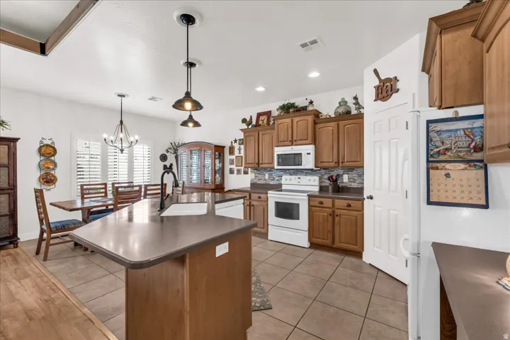 Kitchen featuring wood cabinetry, white appliances, a tile backsplash, and a central island with an undermount sink