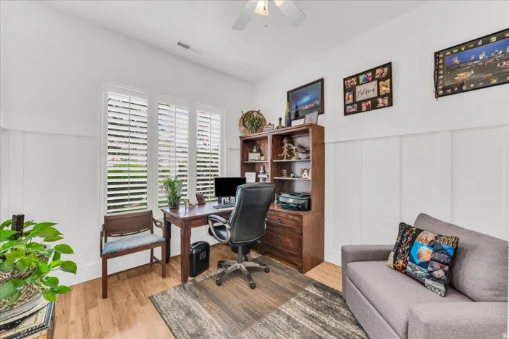 Board and batten wall detailing, wood-finish flooring, white plantation shutters, and a ceiling fan