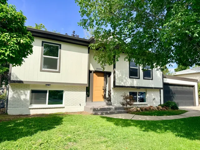Split-level residence featuring white brick and siding exterior, dark trim accents, a wood-finish front door, and an attached garage with a dark door