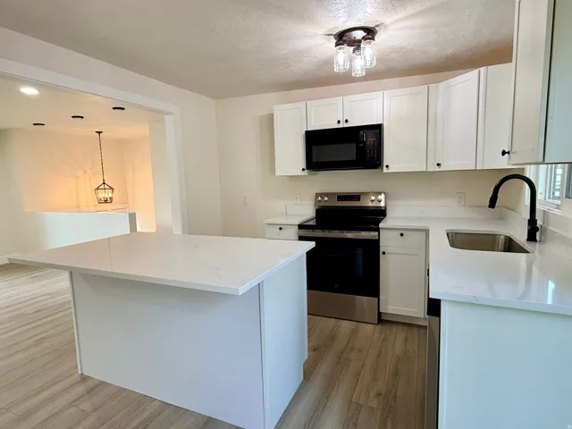 White cabinetry with dark hardware, quartz countertops, stainless steel appliances, wood-finish flooring, and a kitchen island