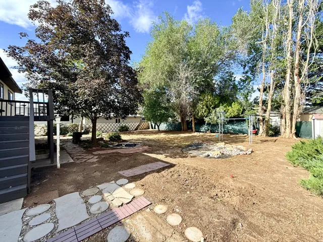 Expansive outdoor space featuring a large tree, raised deck with dark railing, stone and paver pathways, and an established fire pit area