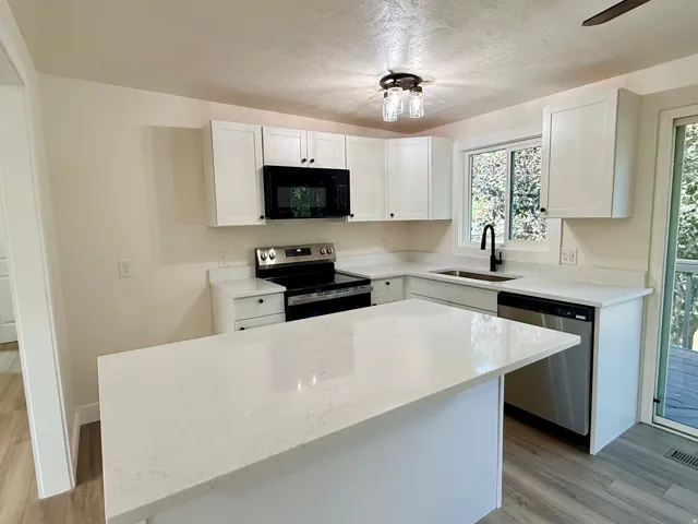 Kitchen featuring white cabinetry, light-toned countertops, a center island, stainless steel appliances, and wood-finish flooring