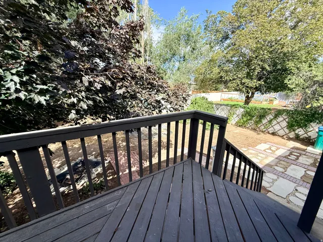 Expansive outdoor deck with dark wood-finish decking and railing, leading to a yard with mature trees and a stone pathway
