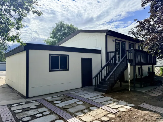 Two-story exterior with a ground-level auxiliary structure, upper-level deck, dark painted exterior stairs, and a decorative paver and stone patio