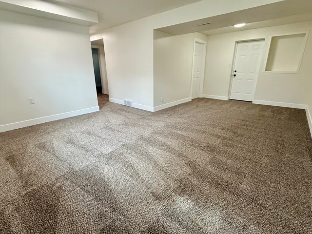Spacious room featuring neutral carpet, white walls, recessed lighting, and a solid core door