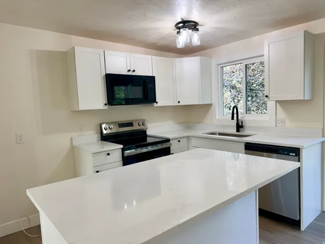Kitchen featuring white shaker-style cabinetry, white countertops, stainless steel appliances, a center island, and a black gooseneck faucet