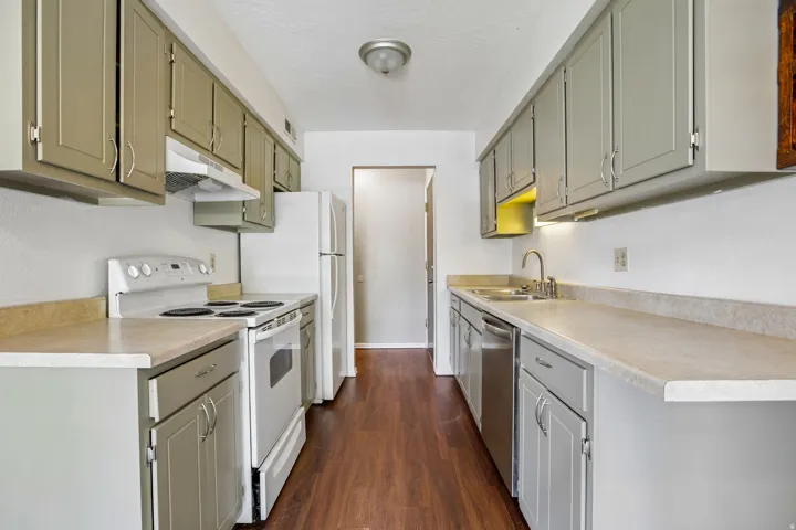 Galley kitchen featuring wood-finish flooring, extensive cabinetry, light-toned countertops, and a full suite of appliances