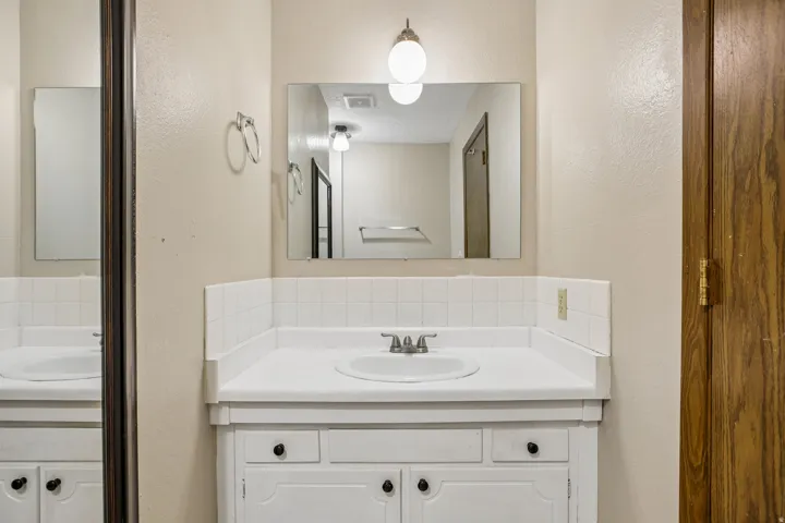 Bathroom vanity with an integrated sink, white cabinetry, and a mirrored wall