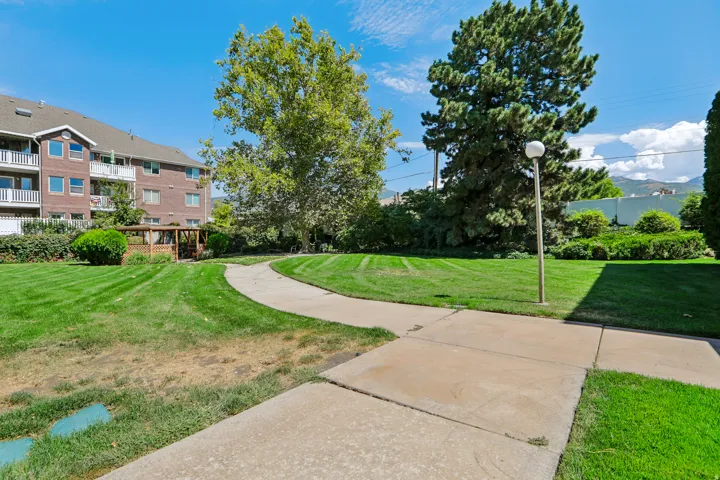 Expansive green space featuring a paved pathway, mature trees, a gazebo structure, and a building with balconies