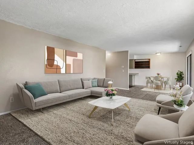 Open-concept living space featuring neutral wall tones, carpeted flooring, and a dining area with a built-in breakfast bar
