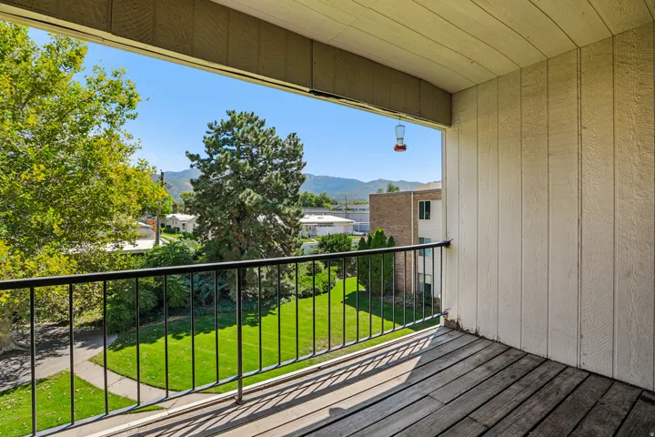 Private balcony with wood-finish flooring, black metal railings, and a tree-lined landscape