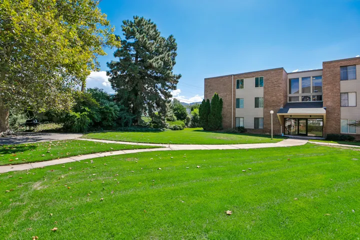 Brick and siding exterior building with multiple levels, expansive lawn, mature trees, and paved walkways