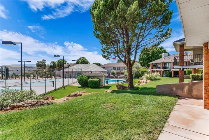 Expansive lawn area with mature trees, fenced tennis courts with lighting, swimming pool, and multiple buildings with balconies