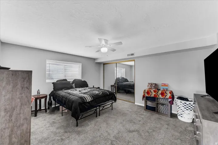 Carpeted room featuring a ceiling fan, a window with blinds, and mirrored closet doors