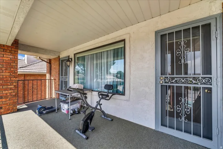 Covered exterior balcony featuring a stucco exterior, brick accent wall, and a gray security screen door with decorative scrollwork