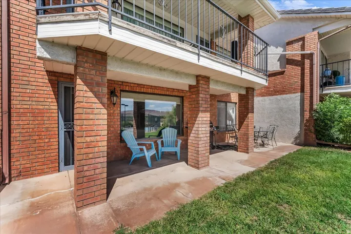 Covered patio area with brick columns, large windows, an exterior light fixture, and a balcony above