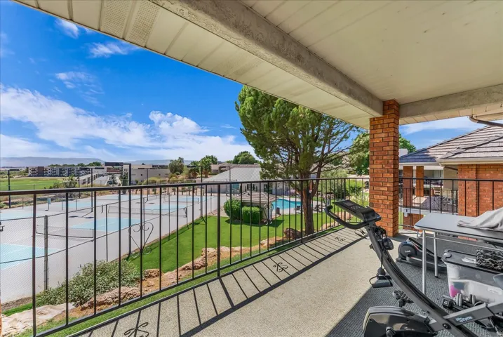 Covered balcony featuring a concrete surface, black metal railing, and brick support column
