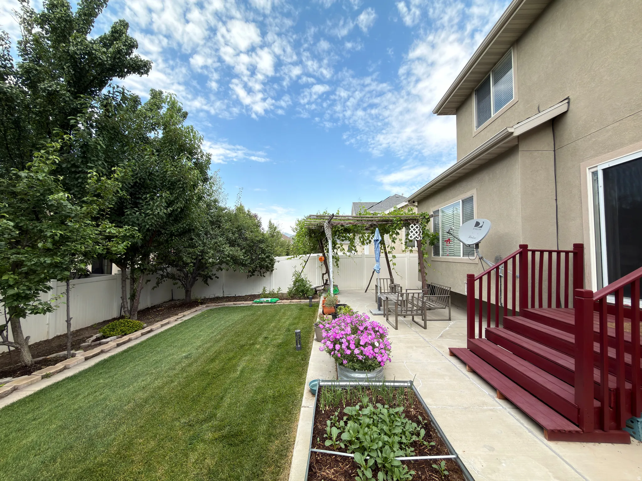 Expansive backyard with a manicured lawn, established trees, and a concrete patio