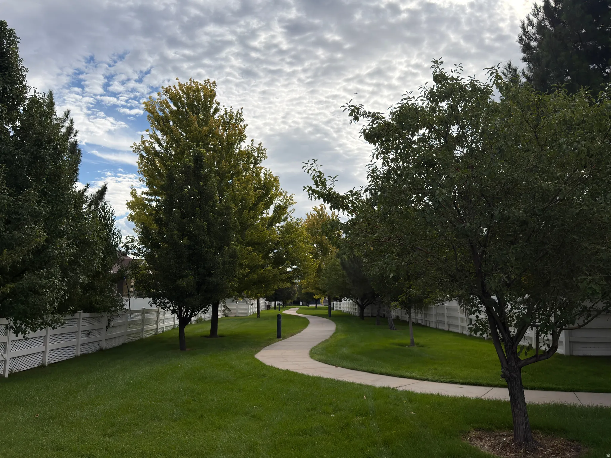 Meandering pathway, surrounded by manicured lawns, mature trees, and privacy fencing