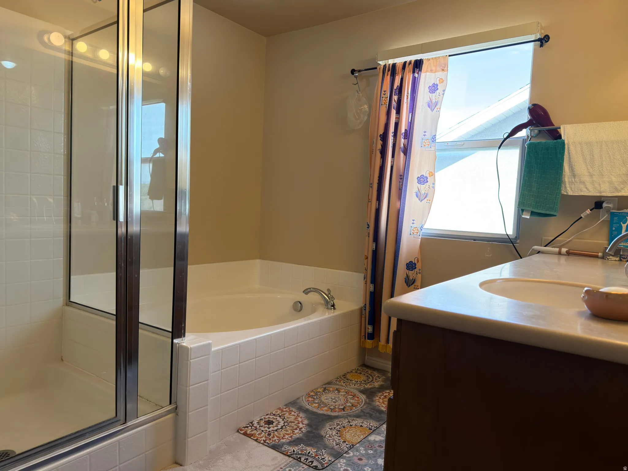 Glass-enclosed shower, jetted soaking tub, single vanity with integrated sink, window with natural light, and tile flooring