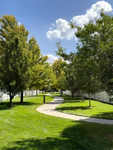 Curved concrete pathway bordered by manicured lawn and mature trees, featuring a white privacy fence