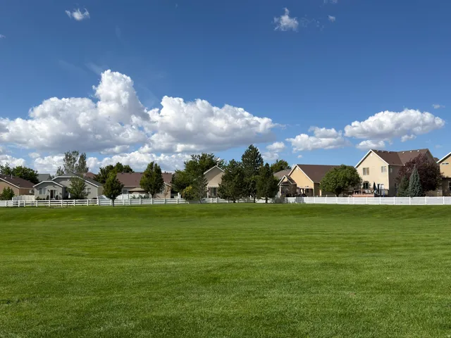 Expansive green space featuring a manicured lawn, established landscaping, and white fencing