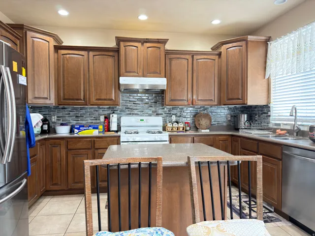 Kitchen featuring wood-finish cabinetry, a central island, stainless steel refrigerator, tile backsplash, and recessed lighting