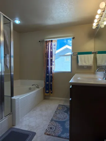 Master bathroom featuring a soaking tub with tile surround, dual vanity with dark cabinetry and quartz countertop, vessel sink, and bright vanity lighting