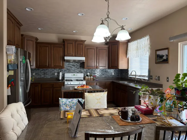Kitchen featuring wood-finish cabinetry, stainless steel refrigerator, white range, tile backsplash, and recessed lighting