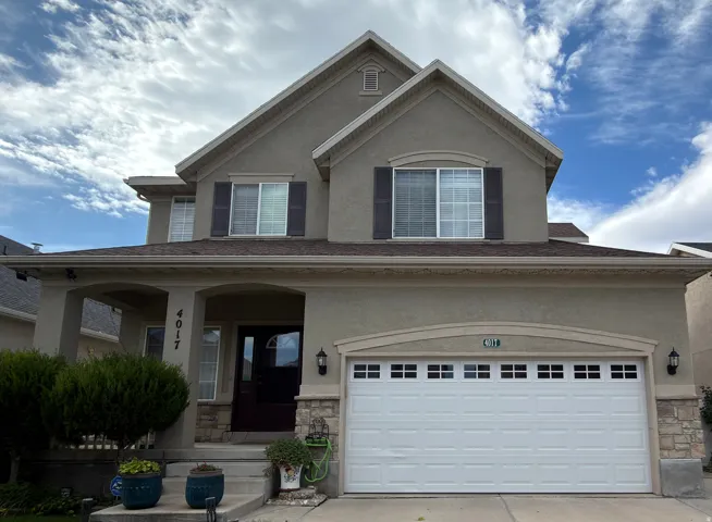 Stucco exterior with stone accents, covered front porch, white paneled garage door with windows, dark entry door, and dark shutters